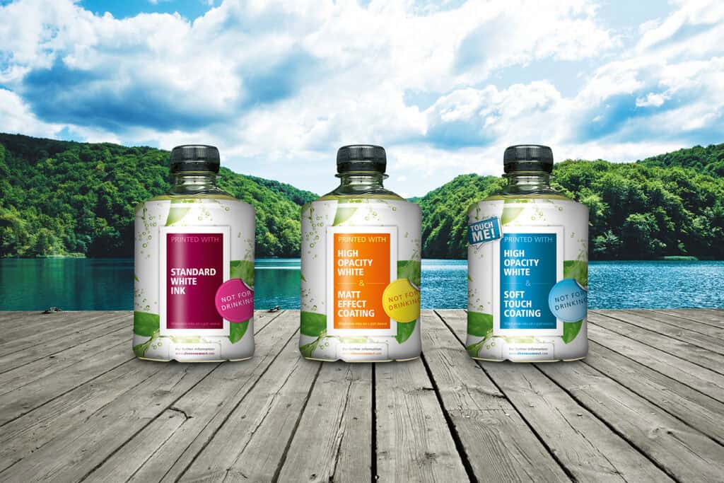 Three PET bottles featuring high-opacity white ink and matte effect coatings developed for the SleeveConnect project on a lakeside setting. Recyclable Shrink Sleeves