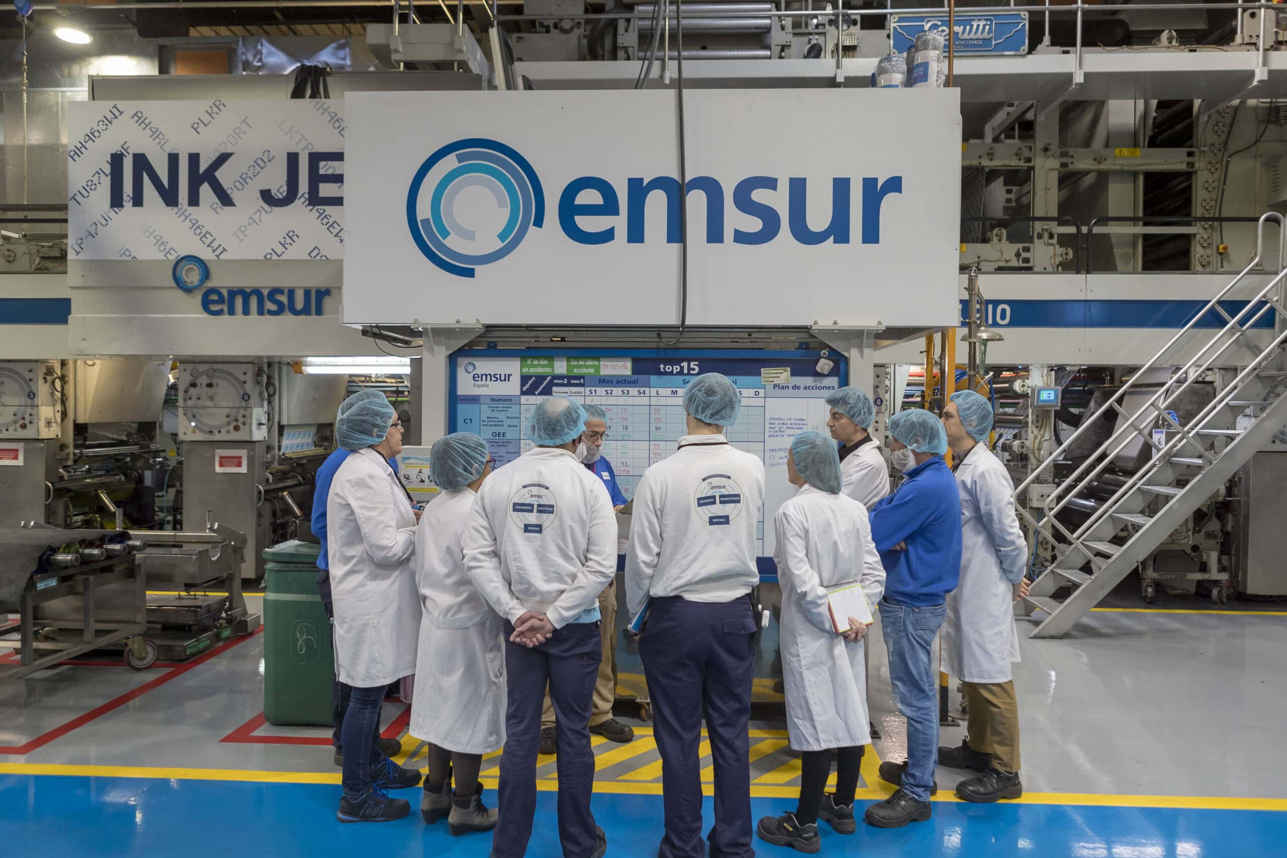 Grupo de expertos en packaging reunidos en la planta de producción revisando indicadores de rendimiento y calidad en un tablero de gestión.