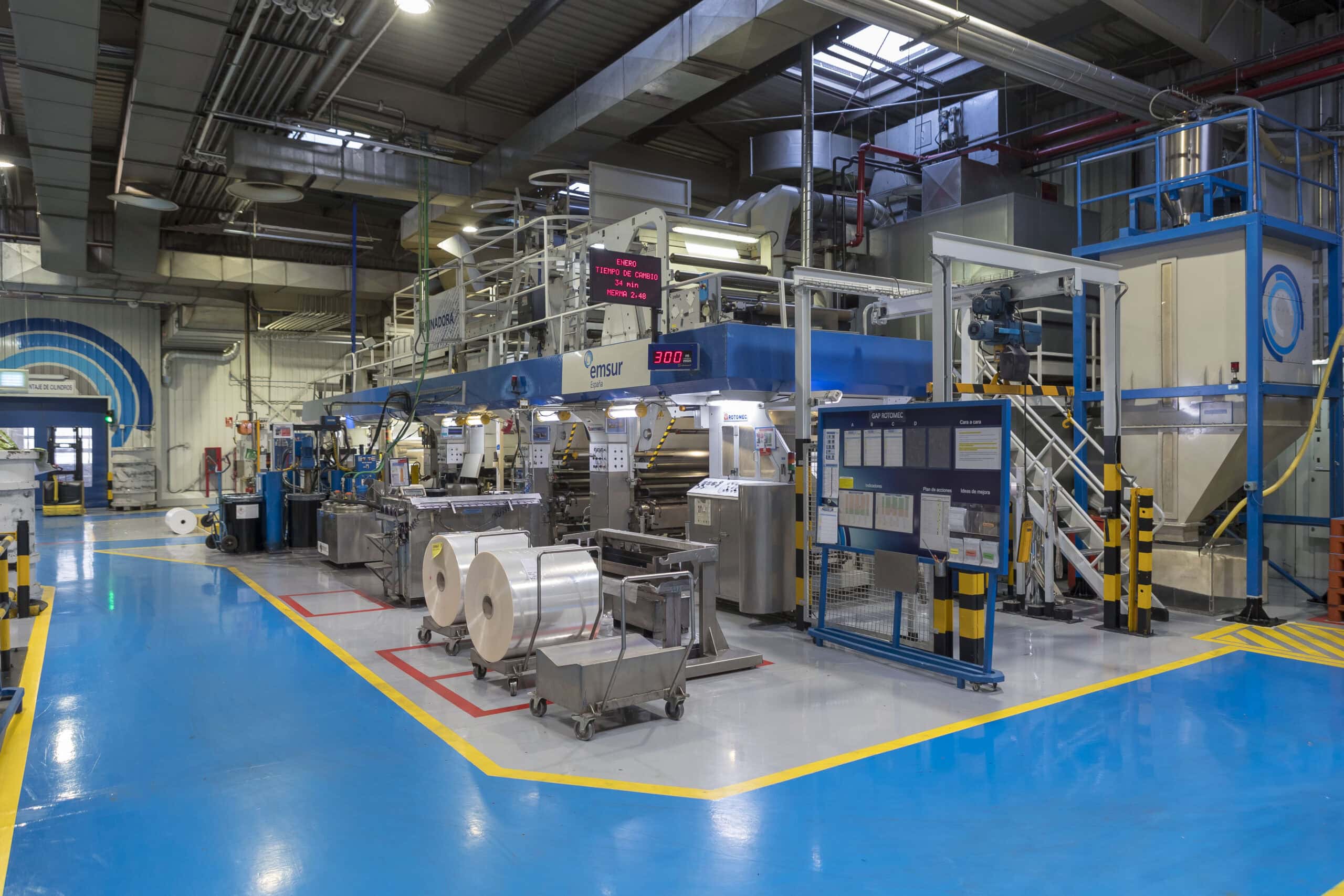 Primer plano de una línea de producción rotativa en funcionamiento, mostrando la complejidad y precisión de las tecnologías de impresión aplicadas a materiales en bobina.
