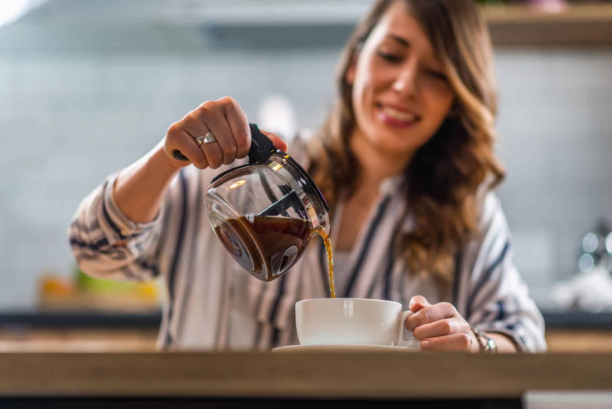 mujer sirviendo café caliente en taza blanca para promoción de empaques de café y empaques para té